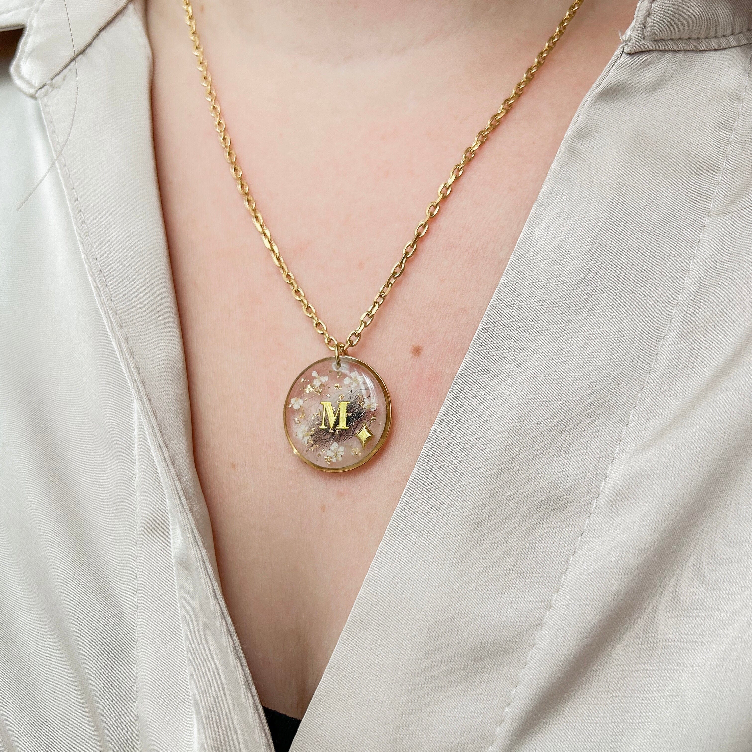 Collier rond en acier inoxydable et résine, diamètre 2 cm, personnalisable avec cheveux, poils d’animaux ou cendres. Possibilité d’ajouter initiales, feuille d’or et symboles au choix.